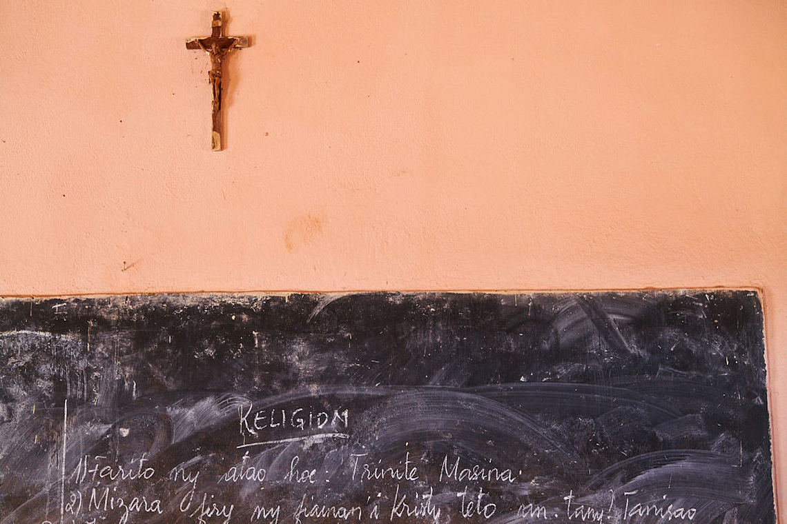 Ein Kreuz, das an der Wand einer schule hängt darunter eine Tafel